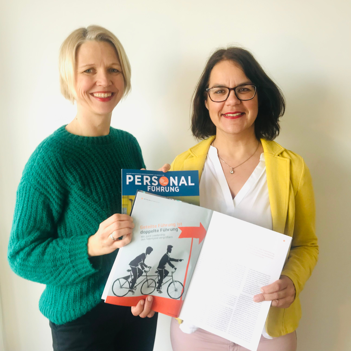Carolin Weigel und Esther HImmen stehen lächelnd mit einem Personal-Magazin in der Hand. Aufgeschlagen ist ihr wissenschaftlicher Artikel über die Studienergebnisse ihrer 360°-Joint LEadership Studie.